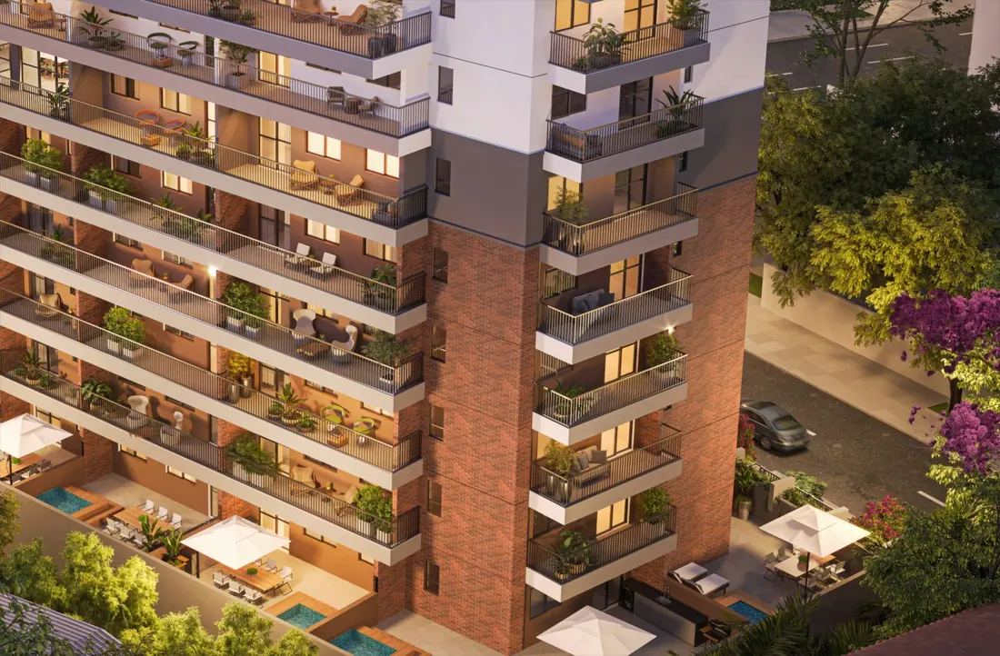 Fachada do Cores da Tijuca à noite, com varandas iluminadas, jardineiras e base em tijolinho